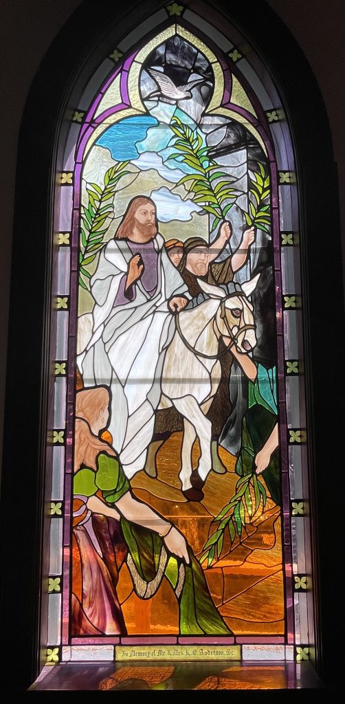 Stained glass window depicting Jesus riding a donkey with a peace dove flying above
